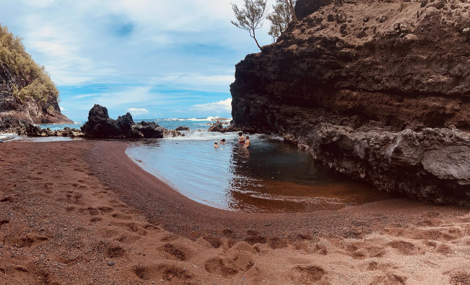 Swimmers in the red sand beach cove near Hana